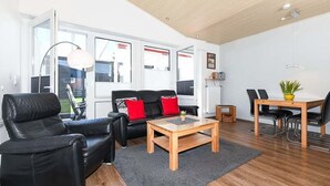 A modern living room with a sofa, coffee table, and dining area. - Vacation cottage Brigitte, Germany (Esens)