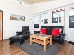 Een moderne woonkamer met een bank, twee fauteuils, een salontafel en een schilderij aan de muur.