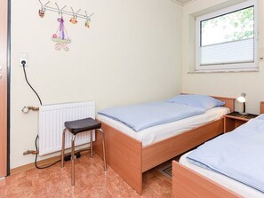 A bedroom with a single bed, a small stool, a radiator, a window, and a wall-mounted light fixture.