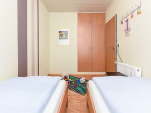 Et værelse med to senge, et skab, en radiator og en legetæppe til børn.