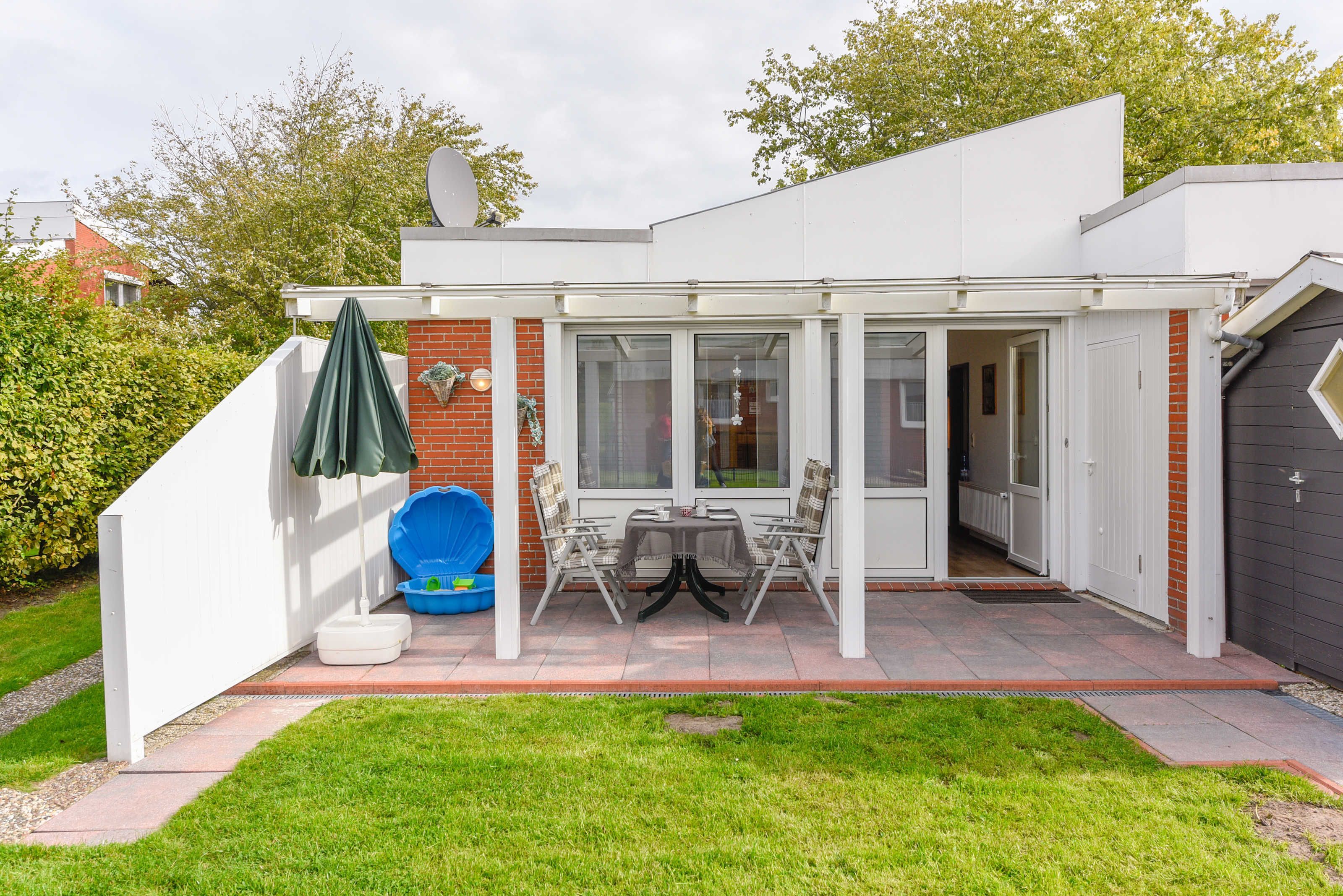 A patio with a table and chairs, a covered area, and a blue container.