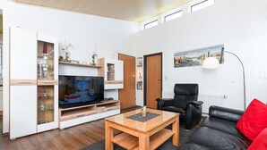 A living room with a TV, a black leather sofa, a wooden coffee table, and a bookshelf. - Vacation cottage Brigitte, Germany (Esens)
