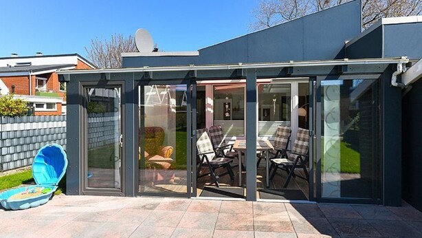 A modern house with a glass-enclosed patio, outdoor furniture, and a satellite dish. - Vacation cottage Brigitte, Germany (Esens)
