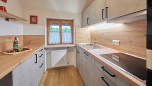 Een moderne keuken met houten kastjes, een ingebouwde oven en een raam met gordijnen.