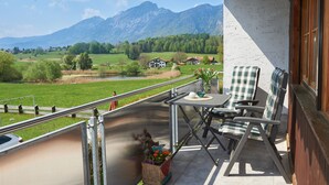 Een balkon met een tafel en stoelen, met uitzicht op een mooi landschap met bergen en huizen.