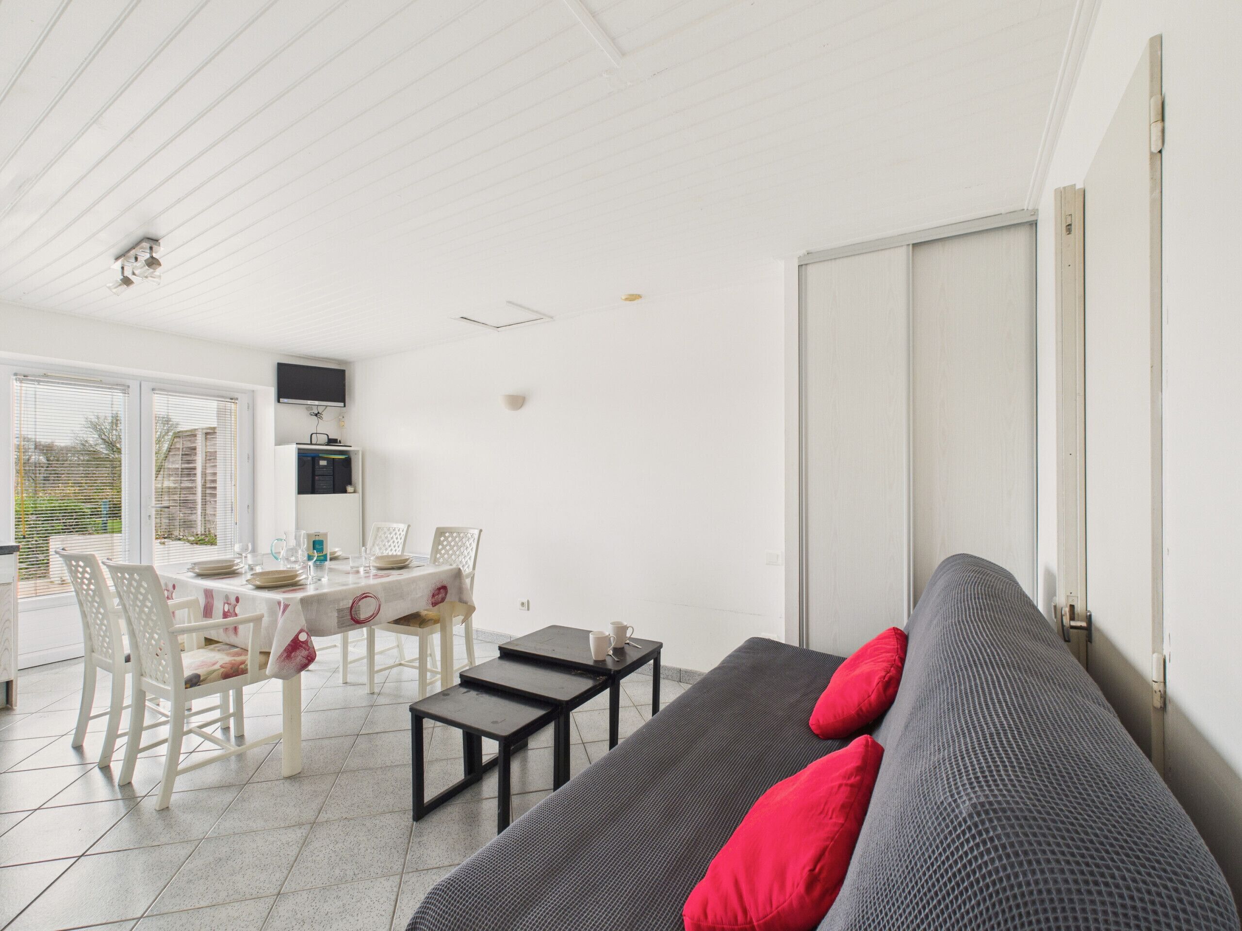 A modern, well-lit room with a dining area, a sofa with red cushions, and a sliding door.