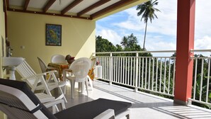 A covered outdoor area with white lounge chairs and a table, a white railing, and a view of greenery and palm trees. - TOP OF VILLA IN ITS VERY GREEN (sainte marie)