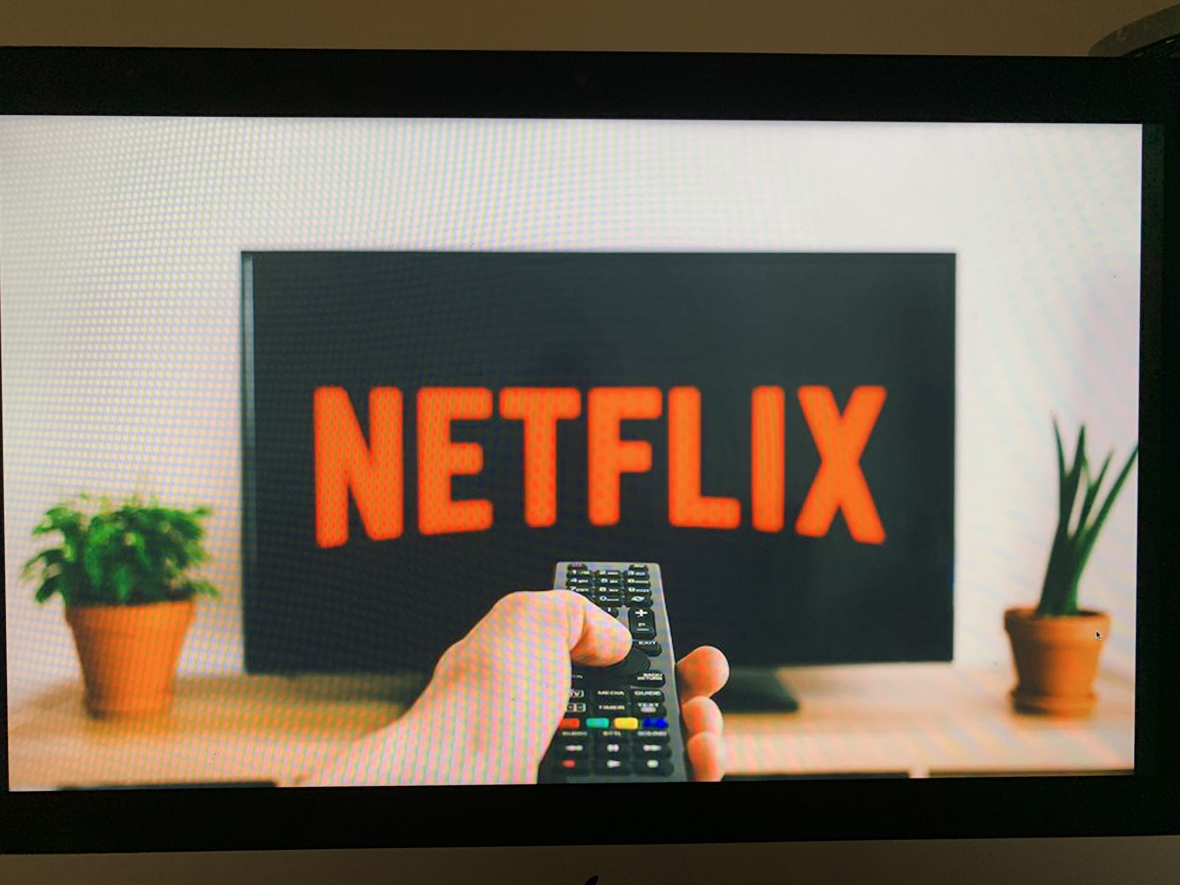 Une main tenant une télécommande devant un téléviseur qui affiche le logo de Netflix.