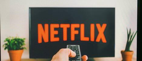 Une main tenant une télécommande devant un téléviseur qui affiche le logo de Netflix.