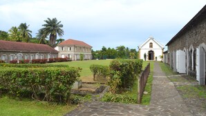 A courtyard with a stone pathway leading to a building with a red roof and a white facade. - TOP OF VILLA IN ITS VERY GREEN (sainte marie)
