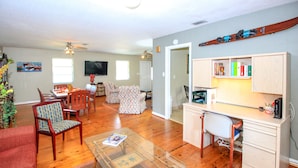 A spacious living room with a wooden floor, a glass coffee table, and a dining area with a TV and chairs.