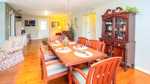 A dining room with a wooden table set for six, surrounded by six chairs. There is a large wooden cabinet with glass doors to the right.