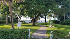 A park with a paved pathway, lush greenery, and a sign indicating it is a HOA members only area with no parking, trespassing, or swimming allowed.