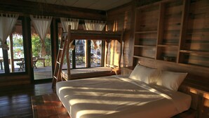 Een slaapkamer in een houten hutje, met een bed, een raam met gordijnen en uitzicht op de natuur.