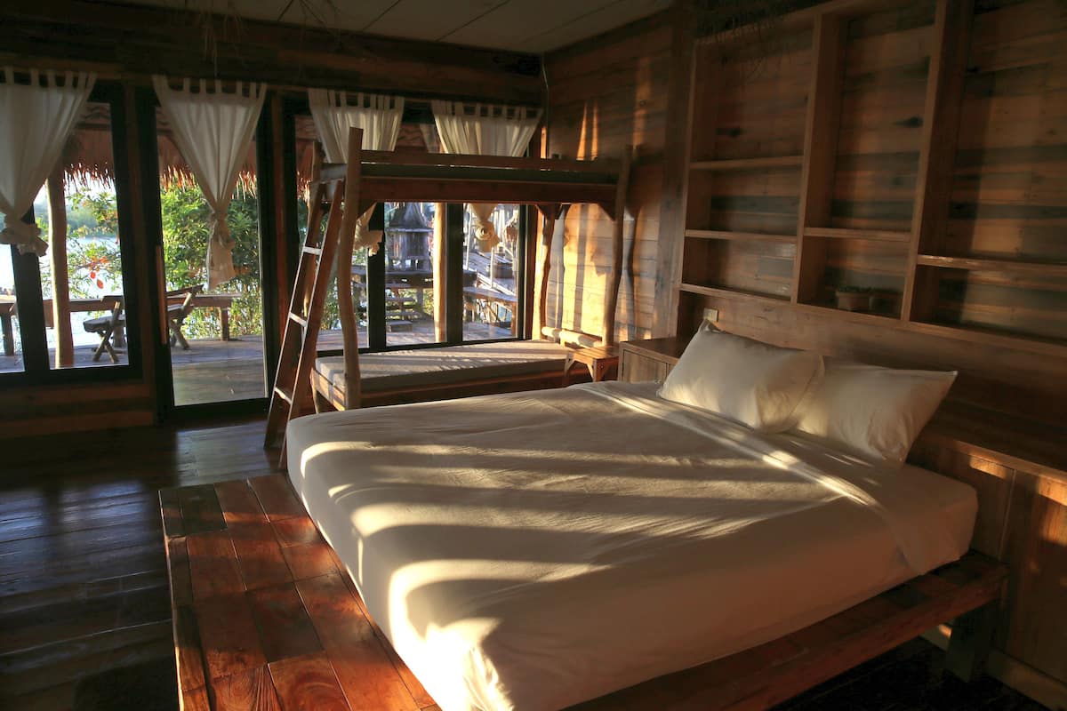 A wooden cabin bedroom with a bed, a window with curtains, and a view of the outdoors.