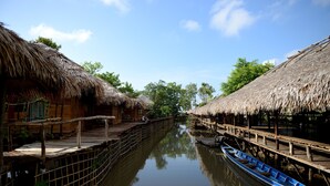 Een rustige rivier met rieten huisjes aan beide oevers, houten looppaden en een roeiboot afgemeerd aan de rechterkant.