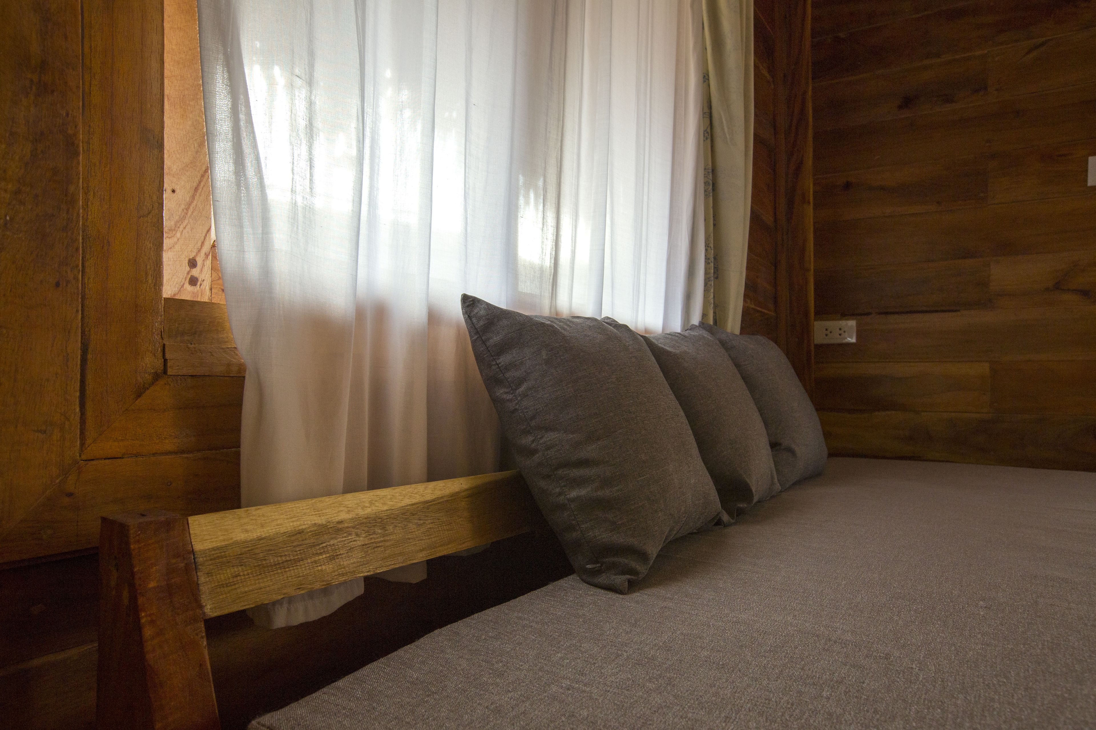 A wooden cabin interior with a bed, a bench, and sheer curtains.