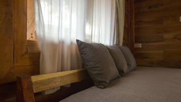 A wooden cabin interior with a bed, a bench, and sheer curtains.