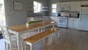 Et moderne køkken med hvide skabe, et træspisebord og en bænk. Et skilt på væggen siger: "THIS IS OUR HAPPY PLACE".