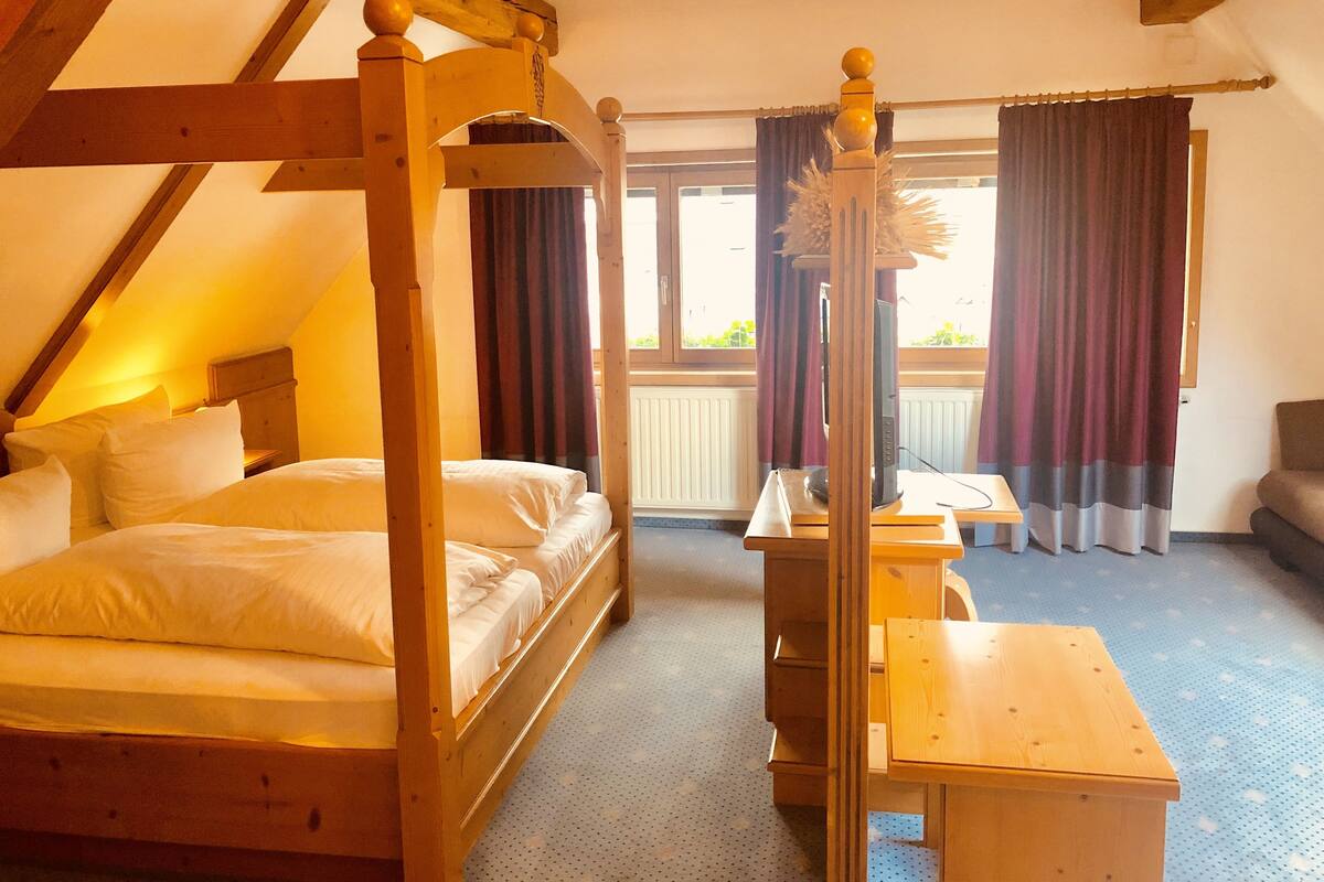 A room with a four-poster bed, a wooden desk, and a window with curtains.