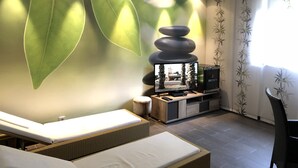 A modern living room with a large wall mural, a television, and a seating area with a massage table. - Hotel Traube (Baden-Baden)