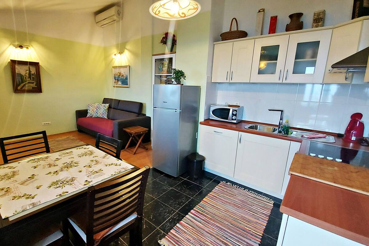 A compact kitchen with a refrigerator, microwave, and sink. There is a dining area with a table and chairs, and a small sofa.