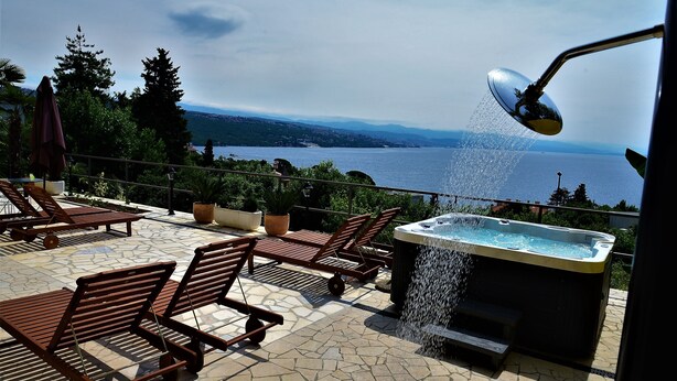 Un patio con sillones de descanso, una bañera de hidromasaje y vistas a un lago.