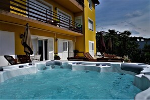 A hot tub area with lounge chairs, a balcony, and a yellow building facade.