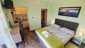 Habitación de hotel compacta con una cama individual, kitchenette pequeño, baño y vista a un muelle.