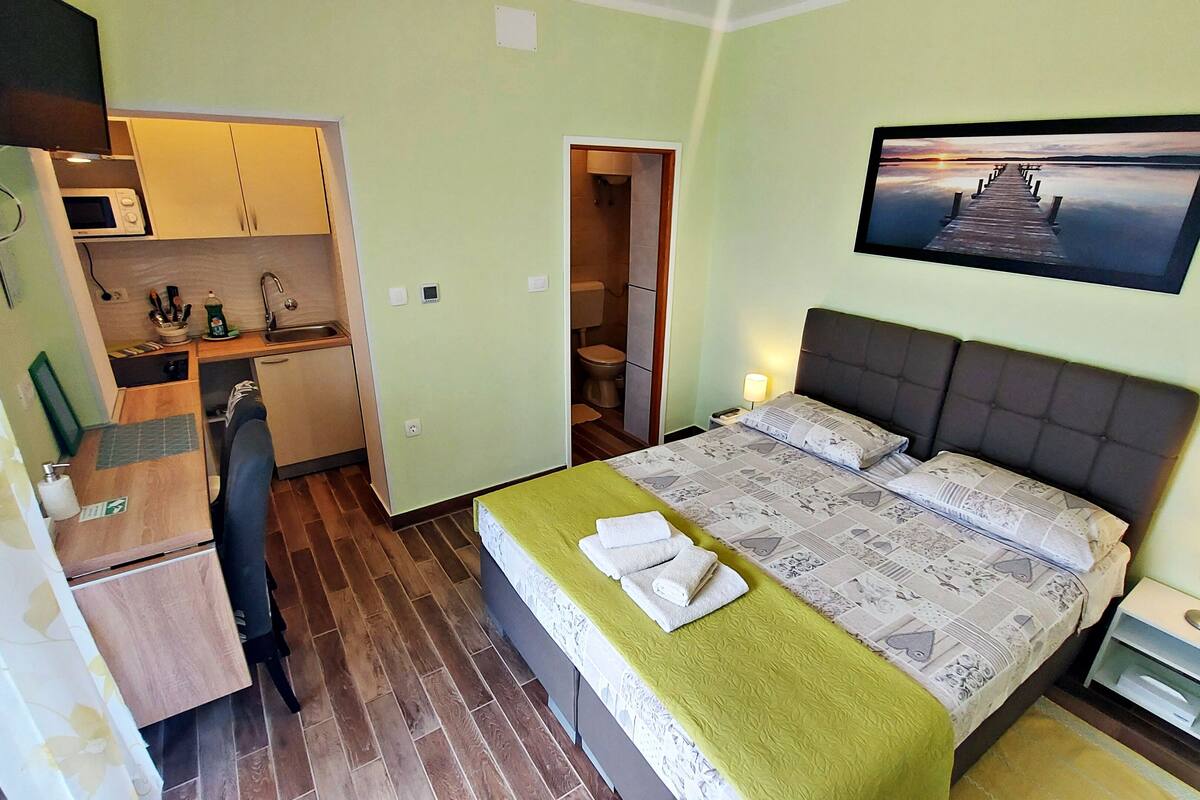 Ein kleines Hotelzimmer mit einem Einzelbett, einer Kochnische, einem Badezimmer und Blick auf einen Steg.