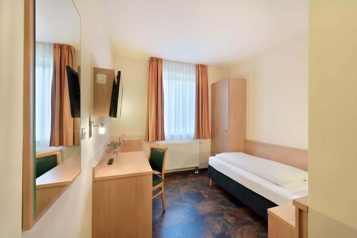 A hotel room with a bed, a desk, a chair, a mirror, a TV, and a window with curtains.
