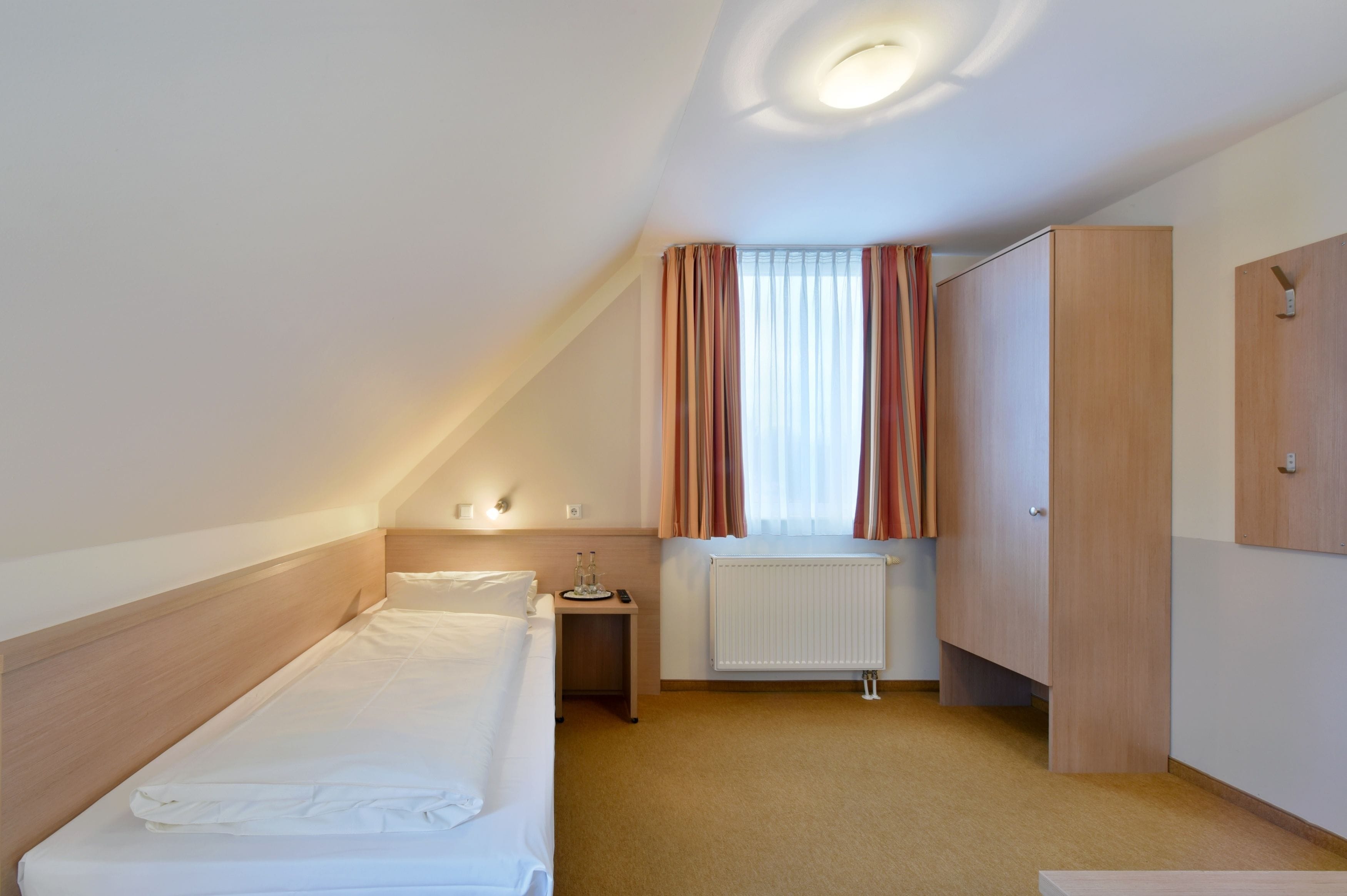 A hotel room with a single bed, a nightstand, a radiator, and a wardrobe.