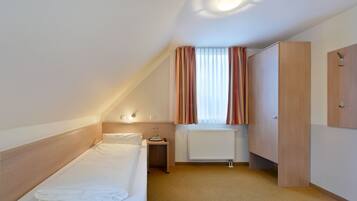 A hotel room with a single bed, a nightstand, a radiator, and a wardrobe.