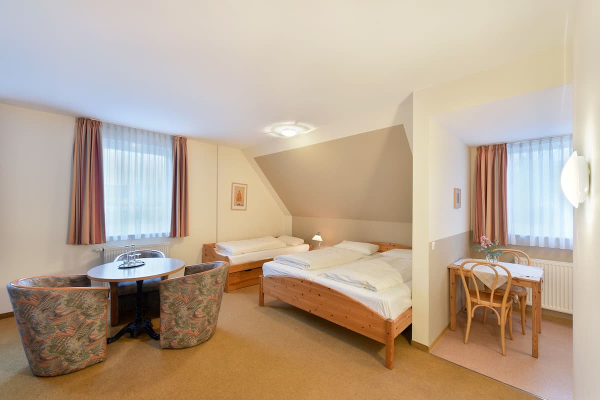 A small, cozy room with a bed, two chairs, a table, and a window with curtains.