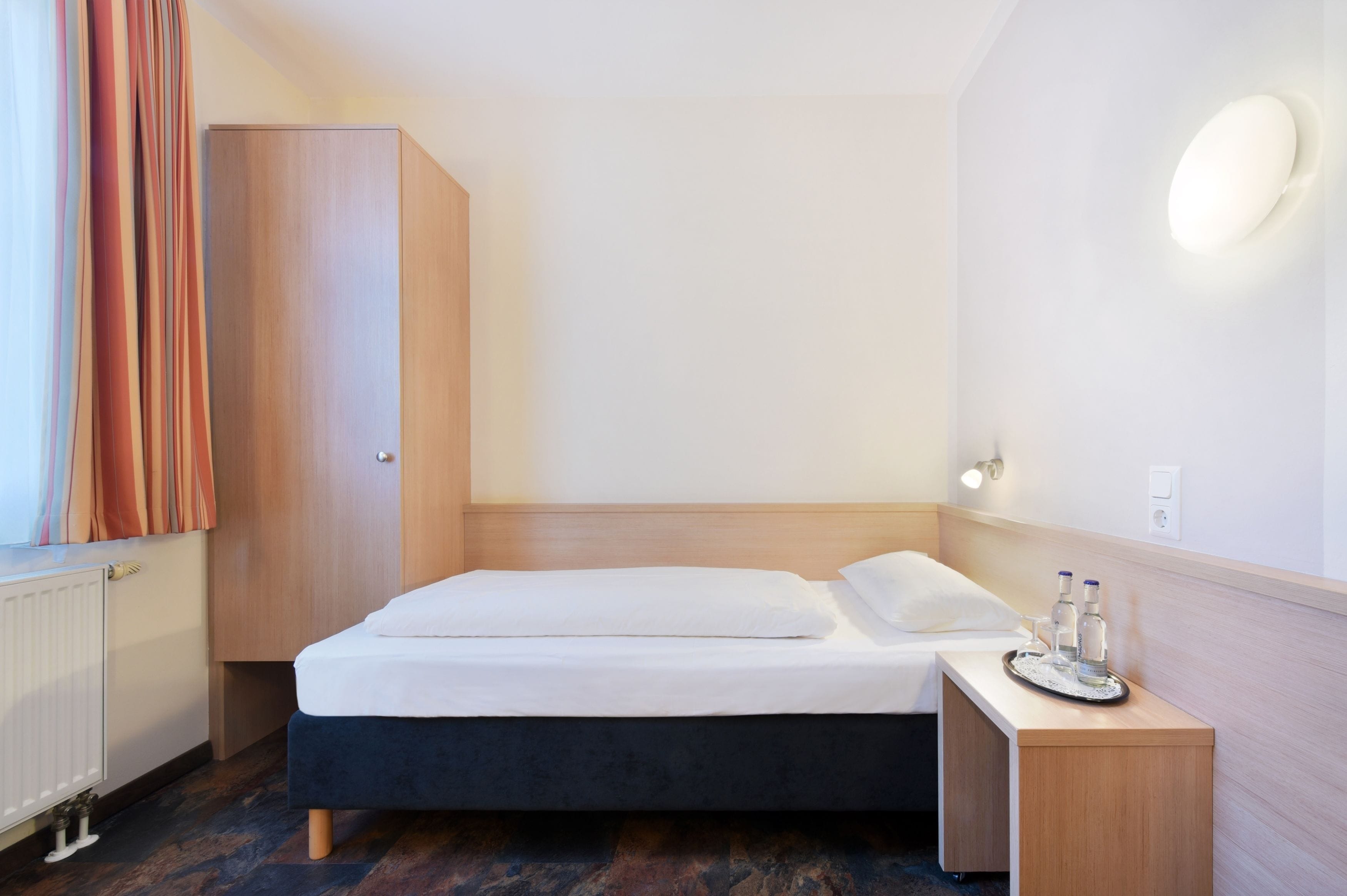 A hotel room with a bed, bedside table, and a wardrobe.
