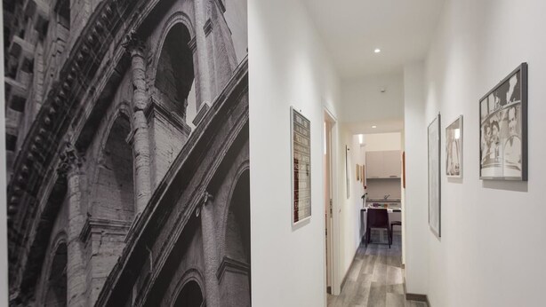 Un couloir avec, au fond, une cuisine moderne, des photographies encadrées accrochées aux murs et une grande fresque murale d’inspiration architecturale.
