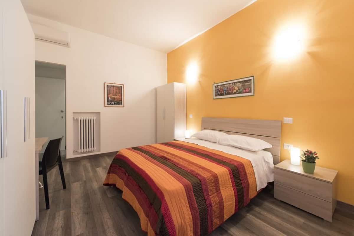 A bedroom with a bed, bedside table, nightstand, radiator, and a chair.