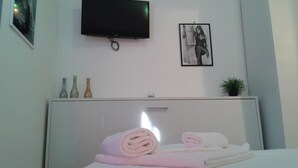 Une chambre d’hôtel avec un lit, un téléviseur à écran plat fixé au mur, un tableau encadré et une petite plante en pot.