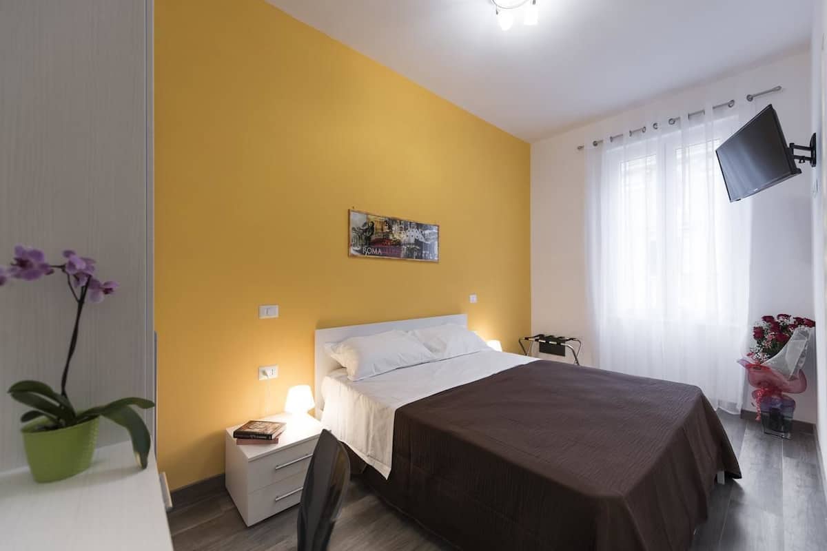 A hotel room with a bed, bedside table, lamp, and a painting on the wall.