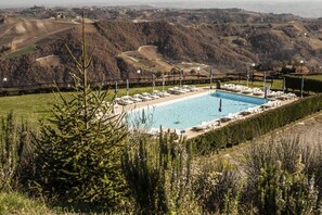A swimming pool with lounge chairs and umbrellas, surrounded by a fence and overlooking a hilly landscape. - Agriturismo Al Castle (Montabone)