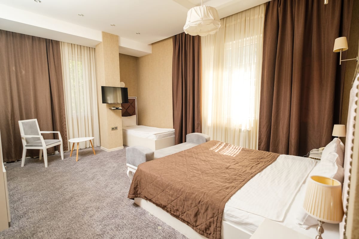 A hotel room with a bed, a desk, a chair, a TV, and a lamp.