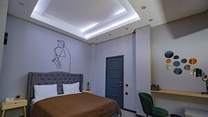 A bedroom with a bed, a desk, a chair, a door, and a wall with circular mirrors. - Maestro Hotel (Baku)