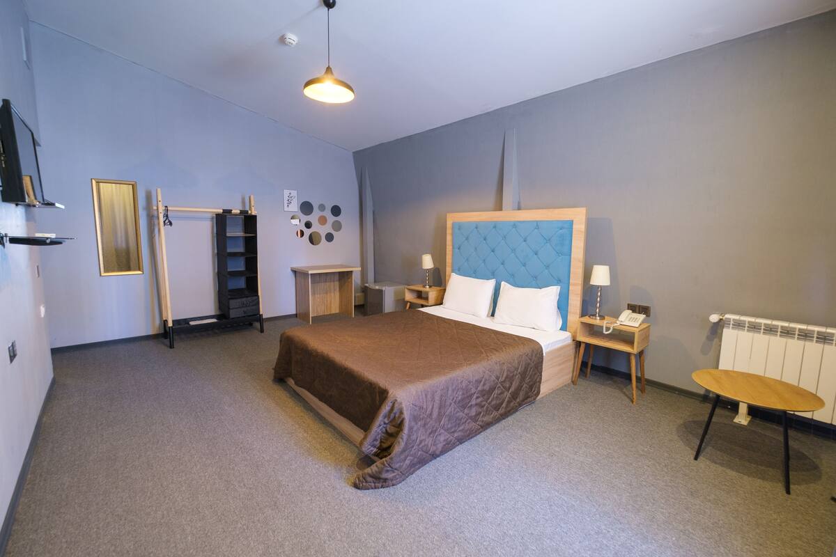 A modern bedroom with a large bed, bedside tables, a desk, and a radiator.