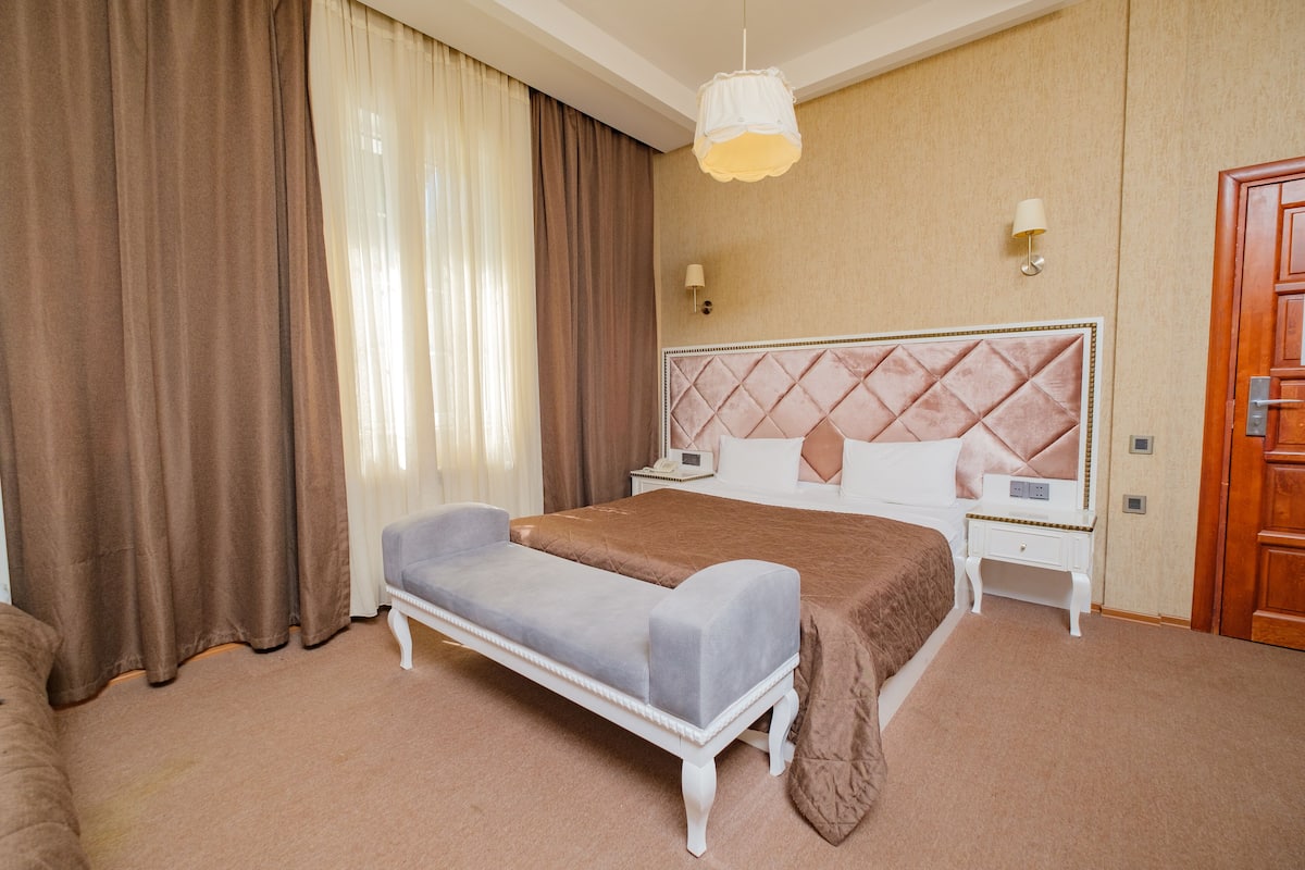 A hotel room with a large bed, a bedside table, a nightstand, a lamp, and a wardrobe.