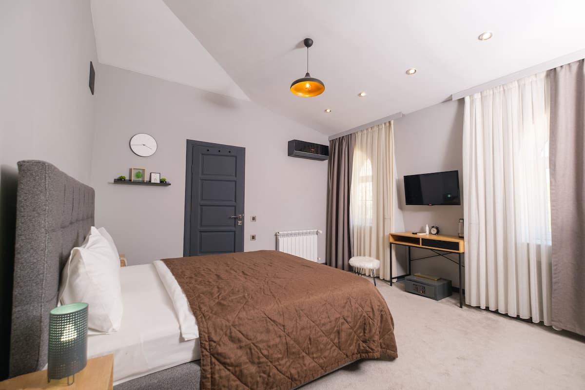 A modern hotel room with a large bed, a desk with a computer, a TV, and a window with curtains.