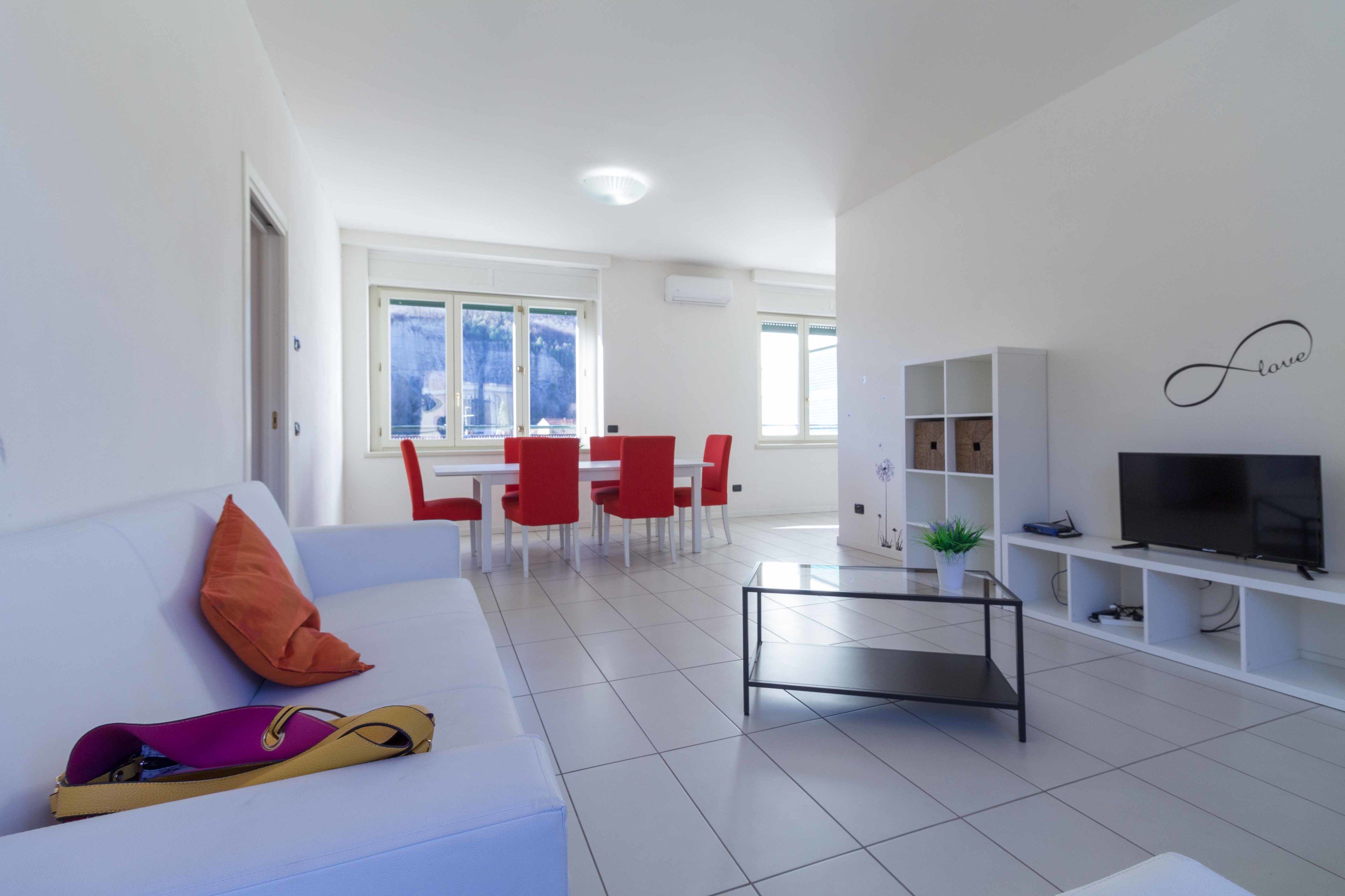 A modern living room with a white sofa, red chairs, a coffee table, and a TV on a white shelf.