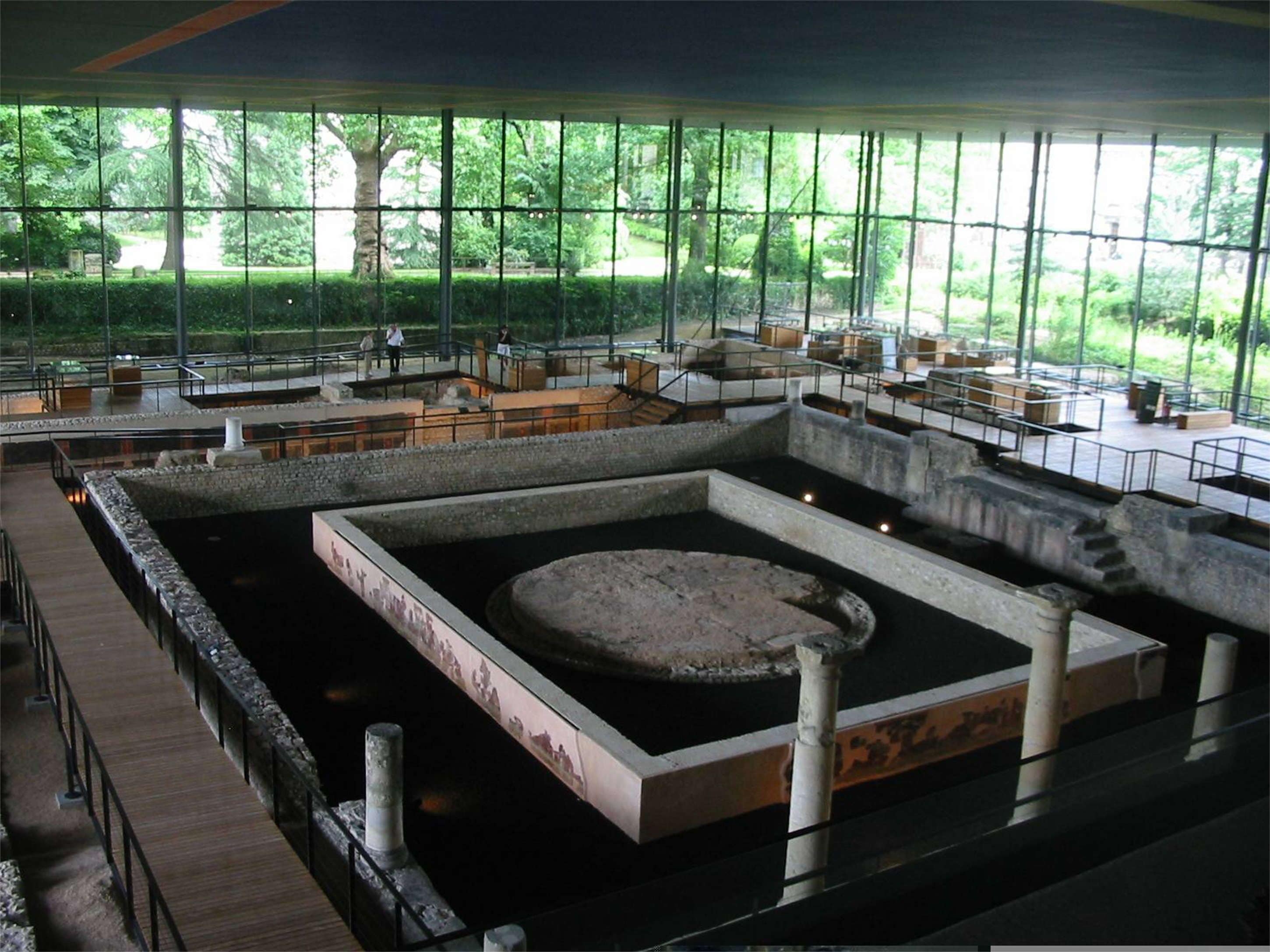 Un sitio arqueológico en interior con varias zanjas de excavación y una poza circular central.