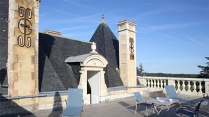 Una terraza en la azotea con un muro de piedra, un pequeño arco y una mesa con sillas.