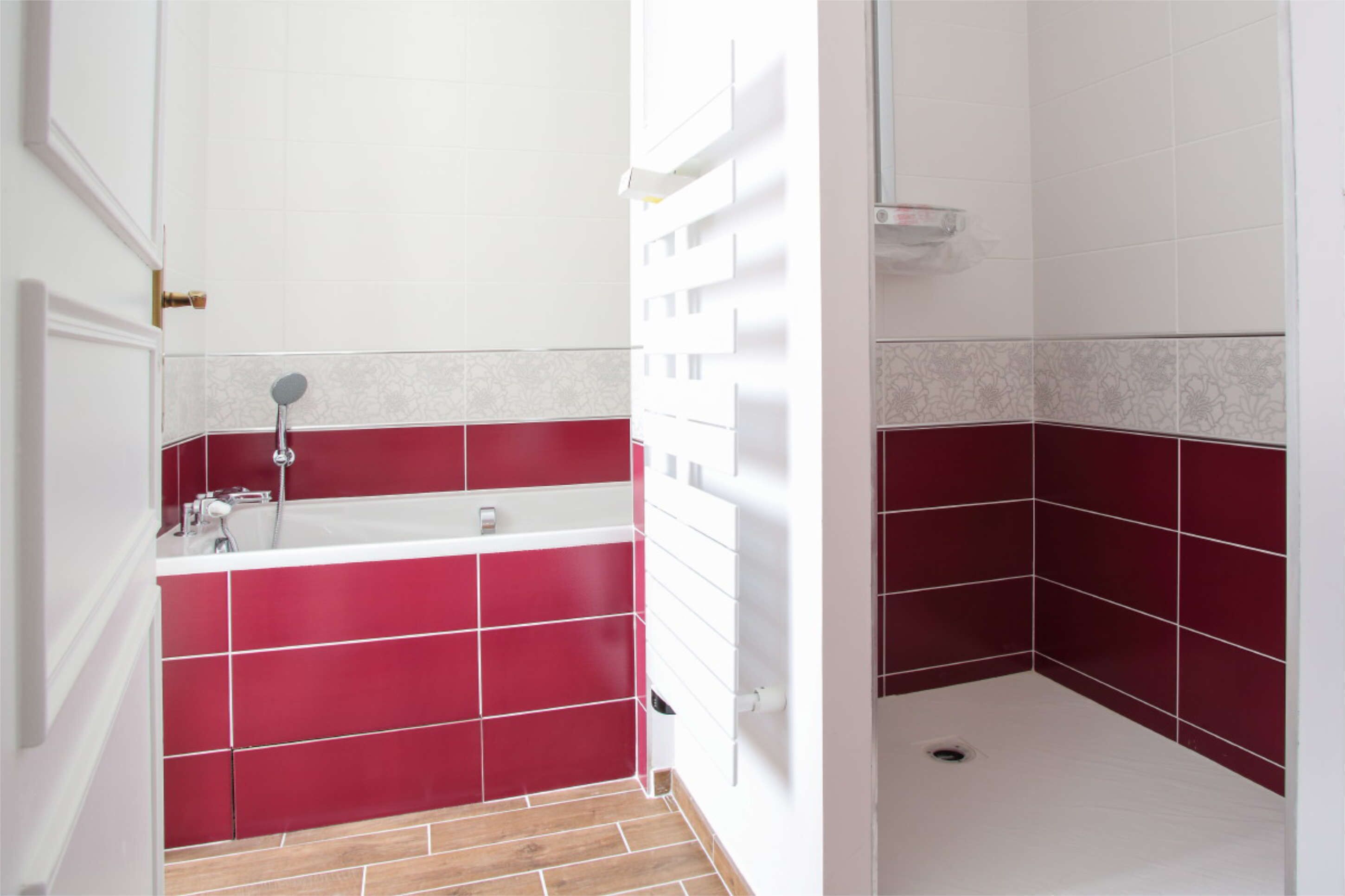 Une salle de bain avec un carrelage aux motifs rouges et blancs, une baignoire, un espace douche et une porte.