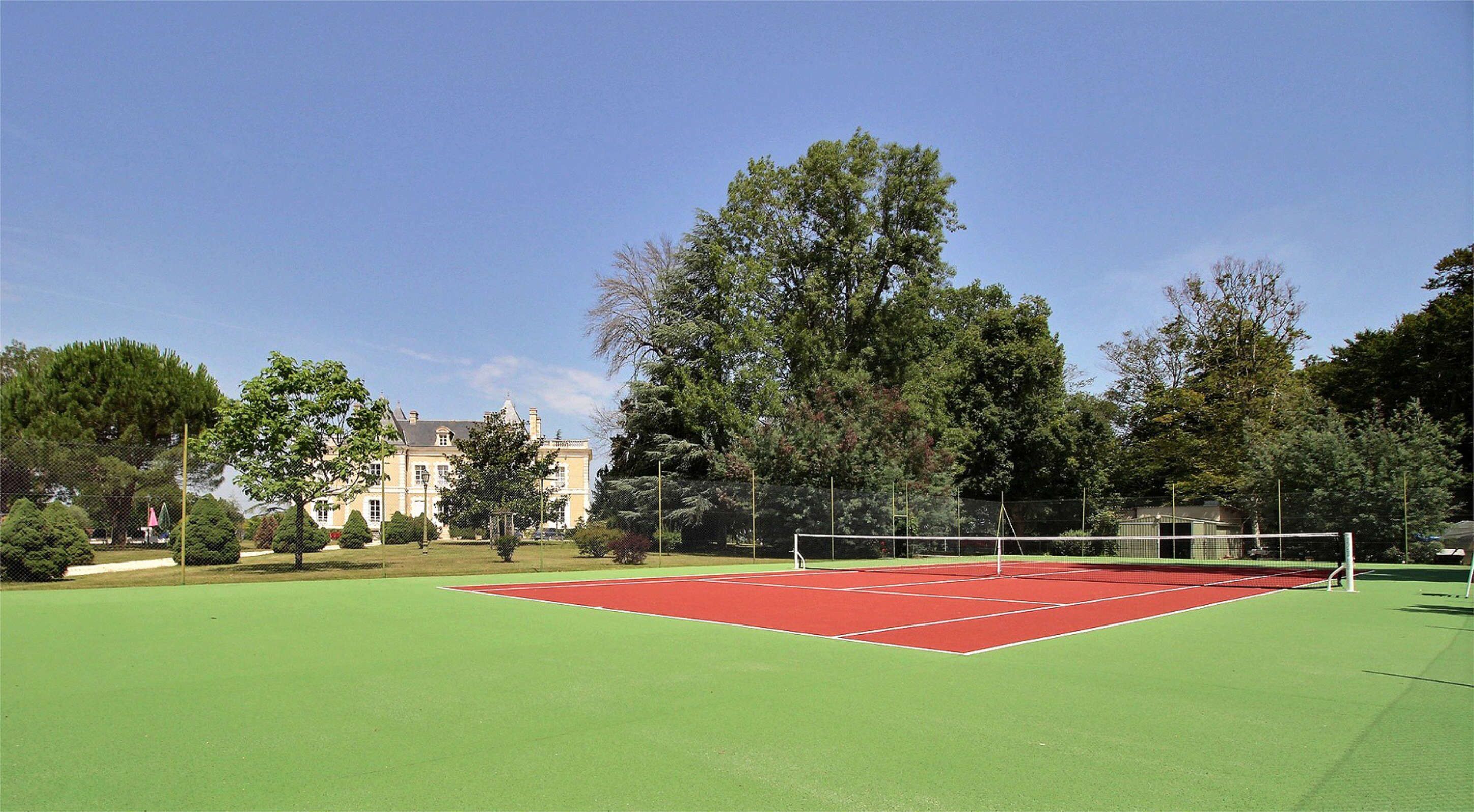 Ein Tennisplatz mit Netz, umgeben von Bäumen und einem Gebäude im Hintergrund.
